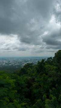 Vertical timelapse footage capturing dramatic storm clouds moving above a tropical mountain forest overlooking a distant city skyline. A cinematic landscape scene ideal for travel.