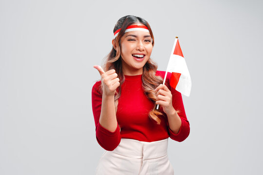 Beautiful young Asian woman is giving thumb up gesture while holding mini country flag.