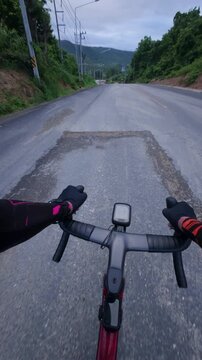 Vertical first-person POV footage of a road cyclist riding along a scenic mountain road at dusk.
