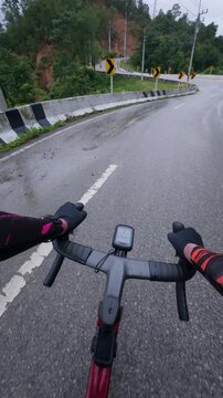 Vertical first-person POV footage of a road cyclist riding through a wet mountain hairpin curve after rainfall. The winding asphalt road, reflective surface.