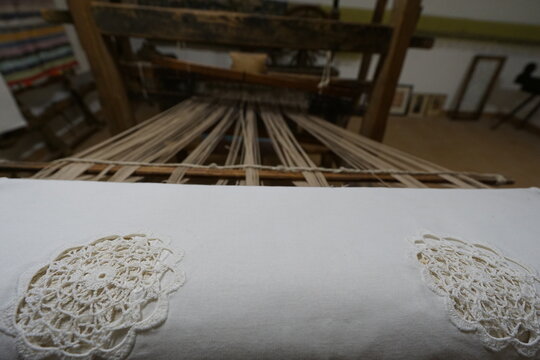 Close-up view of a traditional wooden handloom with white woven fabric and decorative lace motifs, highlighting textile craftsmanship, folk heritage, traditional weaving, and handmade production.