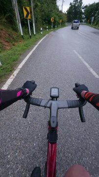 Vertical first-person POV footage of a road cyclist approaching a wet mountain curve surrounded by lush tropical forest after rainfall. The quiet winding road, reflective asphalt.