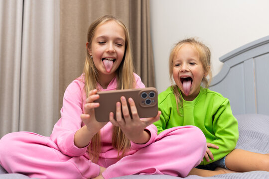 Two young girls making funny faces while watching something on a smartphone at home