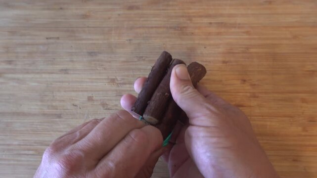 Person taking apart a bundle of fresh licorice root sticks over a rustic wooden board close up