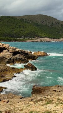 Turquoise blue sea waves breaking on rocky shore at Cala Agulla beach in Mallorca, Spain. Scenic Mediterranean seascape, summer travel destination. 