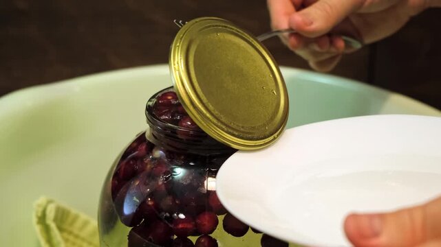 A man canning cherry compote covers a large glass jar with metal lid. Home canning, food preservation, traditional kitchen, winter storage preparations. A Can Seamer. Close-up side view.