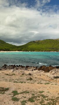 Vertical view of Cala Agulla Beach in Mallorca with visitors relaxing on golden sand and swimming in crystal clear Mediterranean water. Scenic summer destination in Spain.