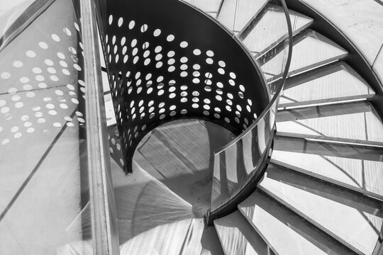Viewed from above, a spiral staircase folds metal railing into sweeping curves across monochrome architecture, while shadows deepen perspective and intensify the geometry