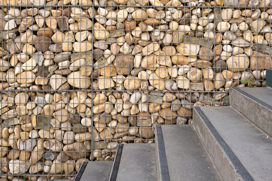 In a close study of material contrast, a concrete staircase meets a gabion wall, while stone texture follows the steps and geometry anchors the exterior architecture