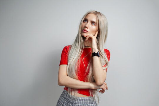 Young pretty blonde girl in red shirt looking thoughtfully away isolated on grey background.