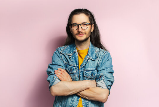 Young confident man with long hair, with crossed hands isolated on pastel pink background.