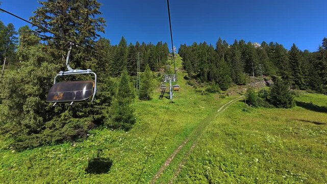 Chairlift ascending through alpine forest beneath Rosengarten peaks, Italy