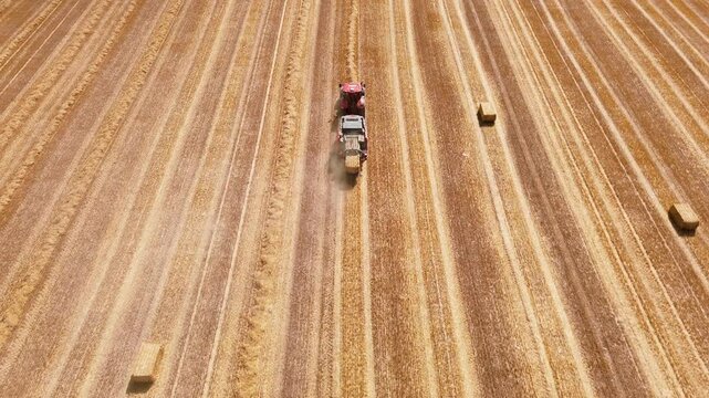 Aerial view of red square baler machinery baling straw on farmland after harvest