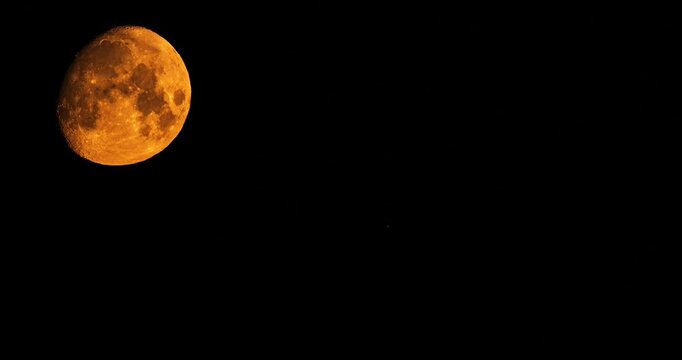 Massive orange moon setting behind tv tower silhouette at night time lapse