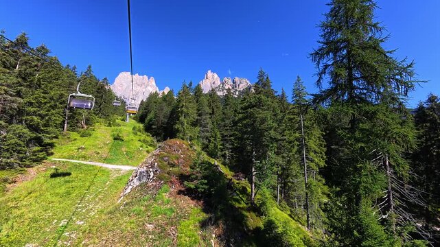 Chairlift ascending through alpine forest beneath Rosengarten peaks, Italy