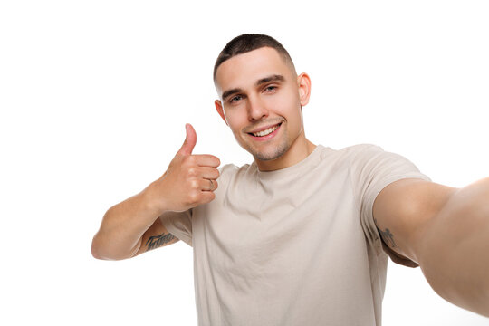 Pretty confident man wear beige t-shirt showing thumb up tacking selfie isolated white background