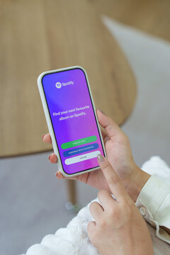 Girl in the room holding a smartphone with Spotify Music app on the screen. Wooden bridge