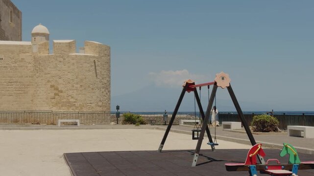 Footage of the historic Brucoli Castle on Sicily's eastern coast, with the faint silhouette of Mount Etna and its volcanic plume visible across the Mediterranean Sea.