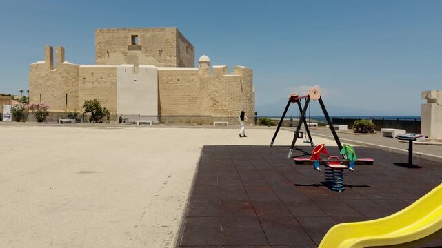 Wide view of Brucoli Castle with children playground, overlooking the Mediterranean Sea with distant Mount Etna on the horizon, Sicily, Italy.