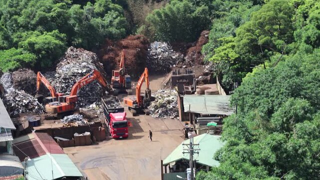 High angle view of a busy scrap metal recycling yard surrounded by trees, 4K b-roll
