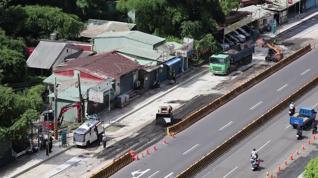 Heavy machinery and workers repaving a highway lane next to old buildings, 4K b-roll