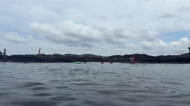 People swimming and relaxing on a rocky reef under a cloudy sky, 4K b-roll