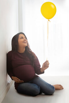 Pregnant woman with a baby bump smiling at the balloon. 