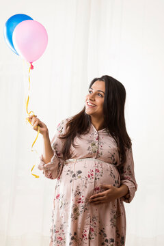 Pregnant woman smiling at the balloons in her hands. 