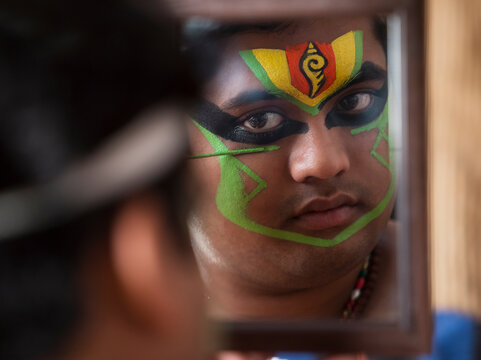 Close up of a Kathakali dancer looking in the mirror and applying green colour on his face. 