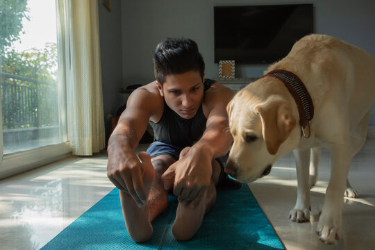 Man doing yoga exercises with his curious dog standing next to him. 