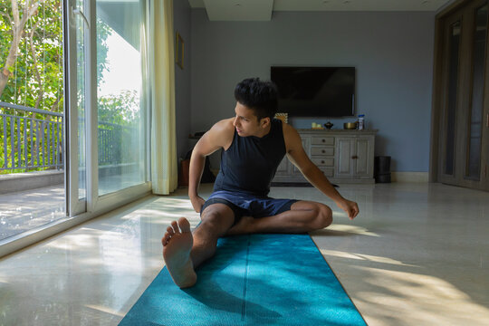 Man sitting on the yoga mat and working out at home. 