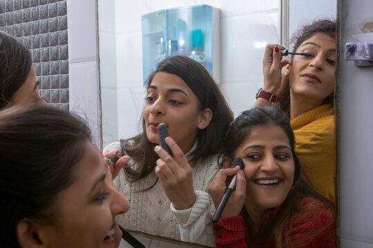 Sisters putting makeup in their faces while looking in the bathroom mirror. 