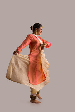 Beautiful kathak dancer performing gracefully over a plain background. 