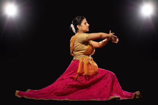 Kathak dancer sitting gracefully and performing in front of a dark background. 