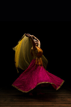 Kathak dancer circling gracefully during a performance in front of a dark background. 
