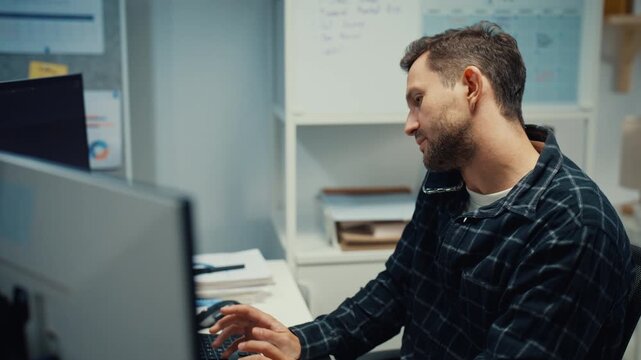 Young Caucasian male developer talk on smartphone while typing coding on computer at office desk. Artificial intelligence software engineering, Cybersecurity database server, Mobile tech call concept.