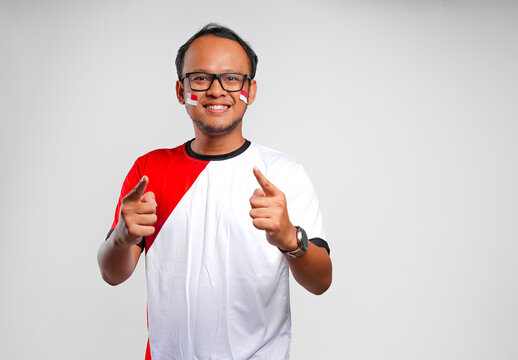 Cheerful young Asian man is smiling while pointing to the camera, isolated by white background.