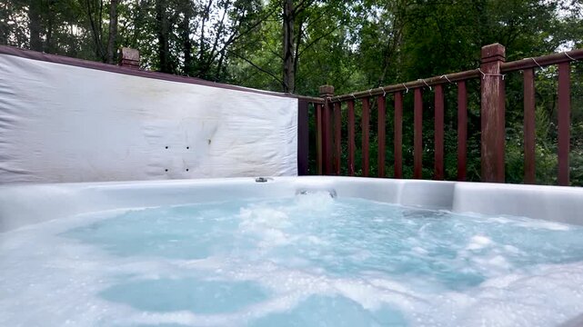 Functioning outdoor jacuzzi with swirling water on a wooden deck surrounded by trees