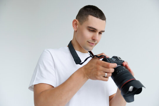 Young man photographer looking on setting at camera on white background