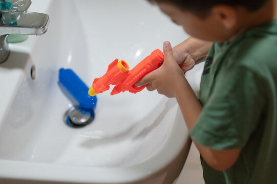 Child Aiming Water Gun at Sink, Engaging in Playful Activity