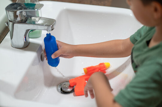 Playful boy experimenting with water toys in a kitchen sink