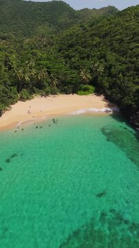 People relaxing in turquoise water at tropical Playa Onda beach in El Valle, Dominican Republic. Aerial drone, vertical format