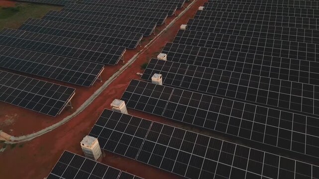 Ground-mounted photovoltaic arrays in Gama, Brasilia, Federal District, Brazil, feature fixed-tilt modules, metal supports and distributed electrical equipment over red soil, drone forward flyover wit