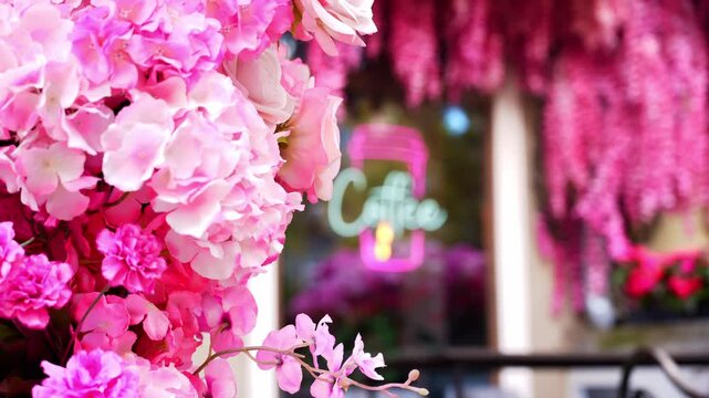 Coffee shop window decorated with pink floral accents and illuminated coffee cup sign on exterior facade. Glowing display attracts attention while decorative elements create welcoming atmosphere in