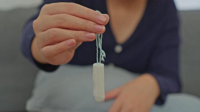 Woman's hand dangling clean white cotton tampon by its blue string