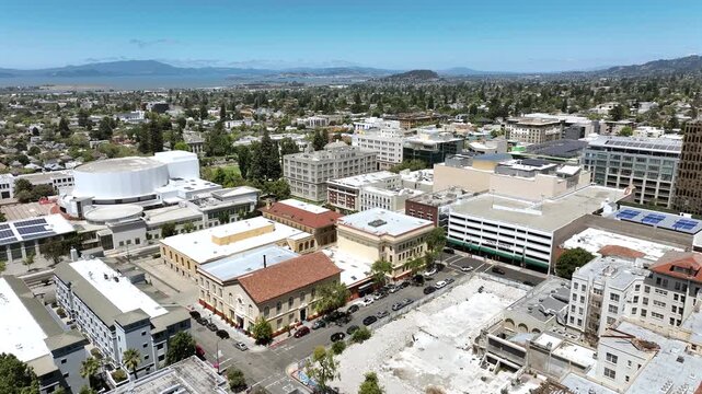 High aerial drone footage of downtown Berkeley, California, featuring commercial buildings, city streets, surrounding neighborhoods, and the rolling East Bay hills in the background.