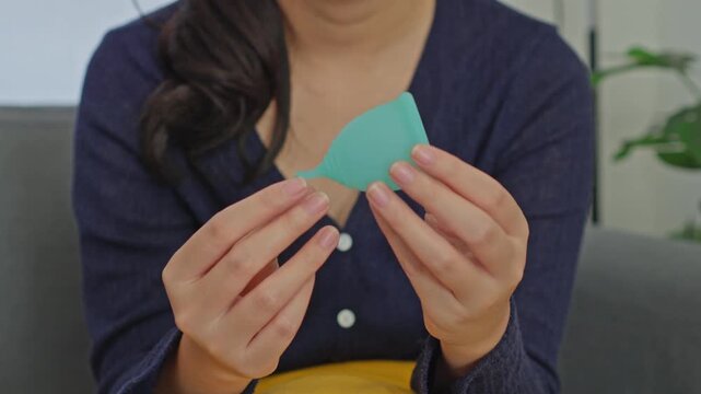 Close-up of woman holding green silicone menstrual cup with both hands while sitting at home