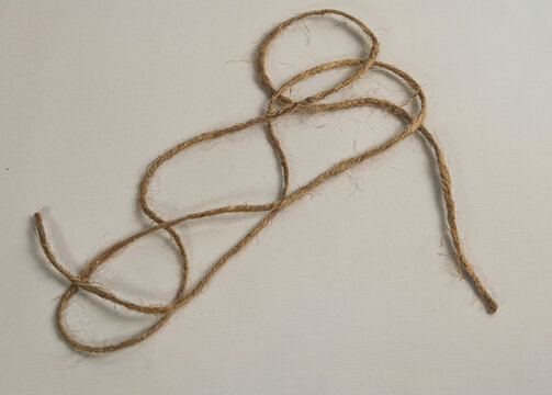 High angle close up shot of eco-friendly brown jute twine string loosely coiled on a clean light grey background, designed for craft, sustainable packaging, DIY, and tying concept materials.