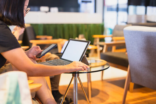 Woman using smartphone while working on laptop in co working space.