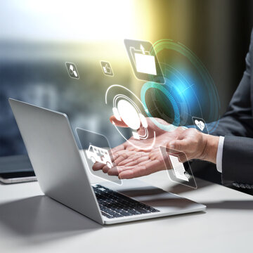 Businessman using laptop with floating holographic icons representing digital customer service, telemedicine, support, and medical assistance. Telehealth and online medical consultation concept